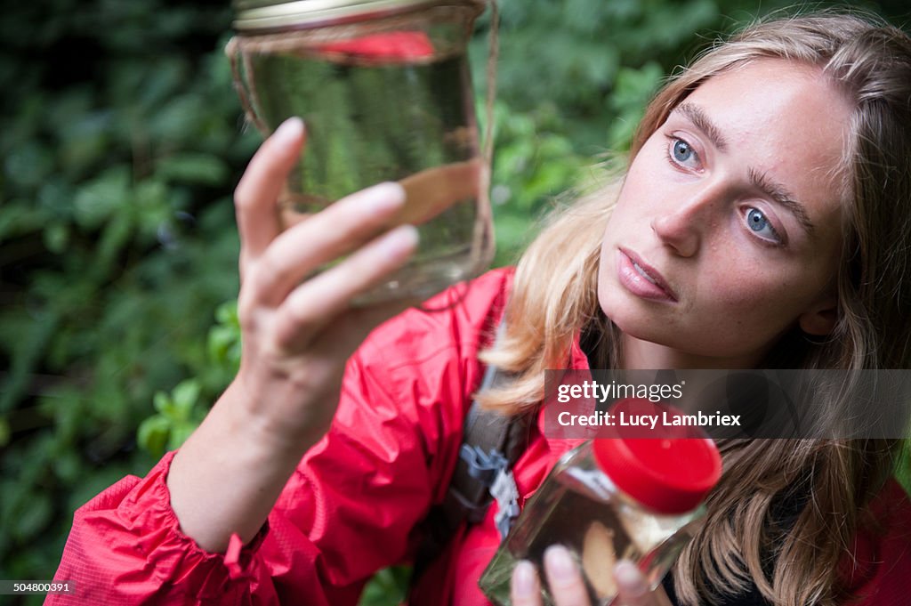 Young woman examining a jar filled with ditchwater