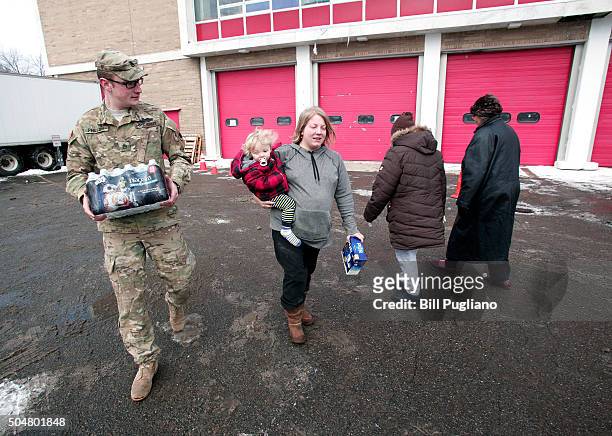 Michigan National Guard Staff Sergeant William Phillips of Birch Run, Michigan, helps Flint resident Amanda Roark and her son Dash take bottled water...