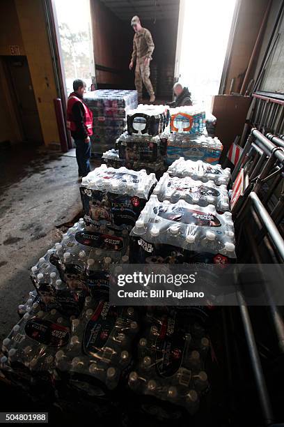 Michigan National Guard Staff Sergeant William Phillips of Birch Run, Michigan, helps a worker unload a pallet of bottled water at a Flint Fire...