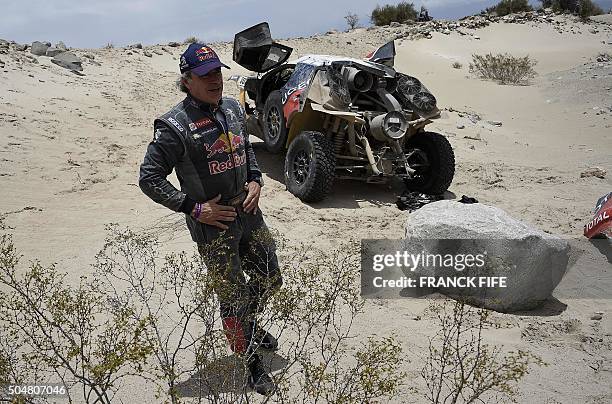 Peugeot's Spanish driver Carlos Sainz stands next to their car after a mechanical failure during the Stage 10 of the Dakar 2016 between Belen and La...