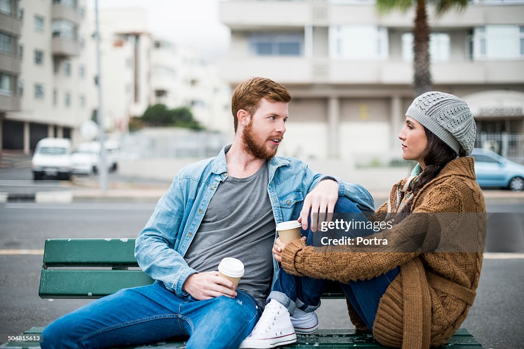 Couple talking while relaxing on bench by street
