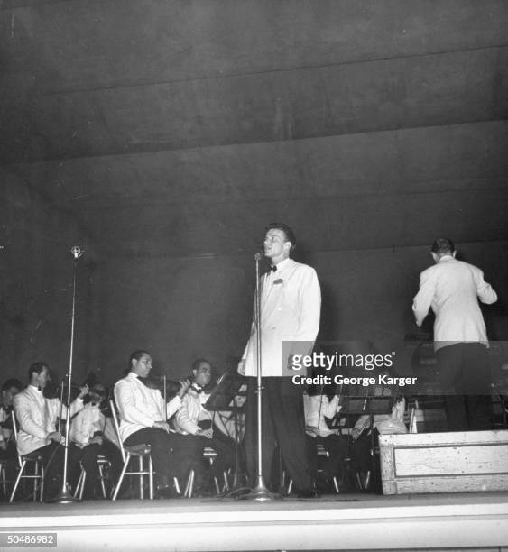 Singer Frank Sinatra rendering a song as conductor Max Steiner leads the New York Philharmonic orchestra during concert featuring the crooner which...