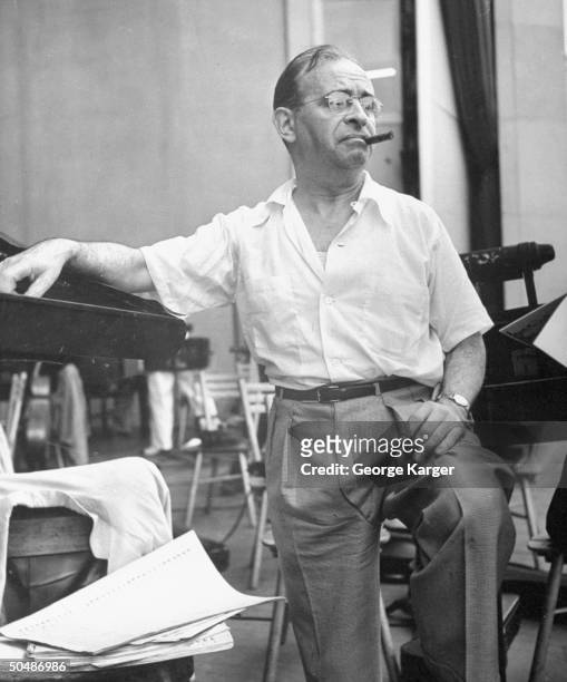 Conductor Max Steiner smoking a cigar while taking a break from conducting the New York Philharmonic orchestra during a rehearsal for singer Frank...