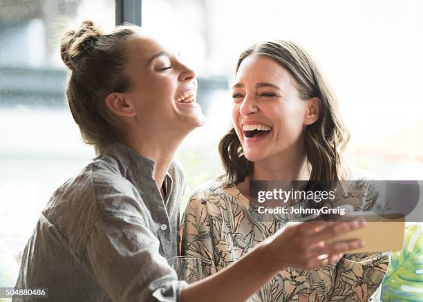 mujer sosteniendo el teléfono móvil con freind, riendo - amistad fotografías e imágenes de stock