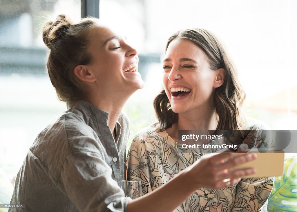 Woman holding mobile phone with freind, laughing
