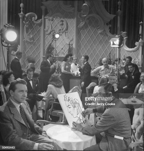 Movie Dir./artist Jean Negulesco drawing a caricature of actor Paul Henreid between takes on the set for his movie The Conspirators at Warner Bros....