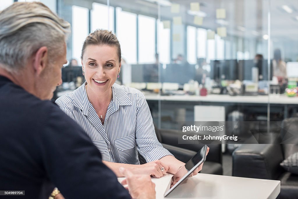 Mid adult busineswoman using tablet with mature man, smiling