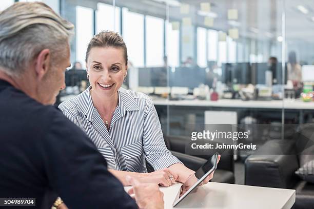 mid adult busineswoman using tablet with mature man, smiling - business relationship stock pictures, royalty-free photos & images