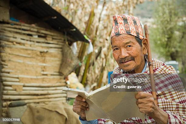 senior man reading book in outdoor and looking at camera. - glimpses of daily life in nepal stock pictures, royalty-free photos & images