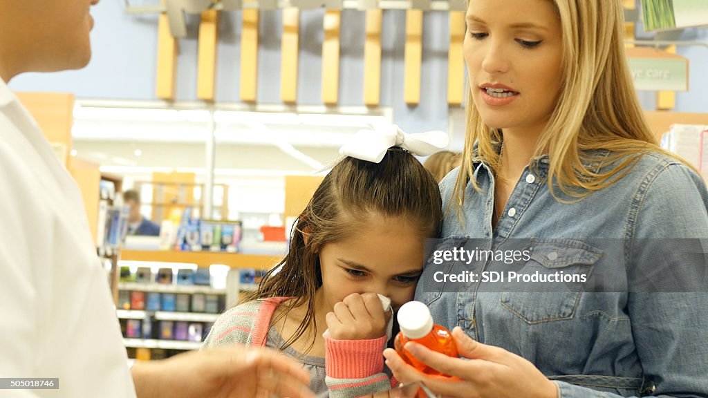 Mother purchasing cold medicine for sick elementary age daughter
