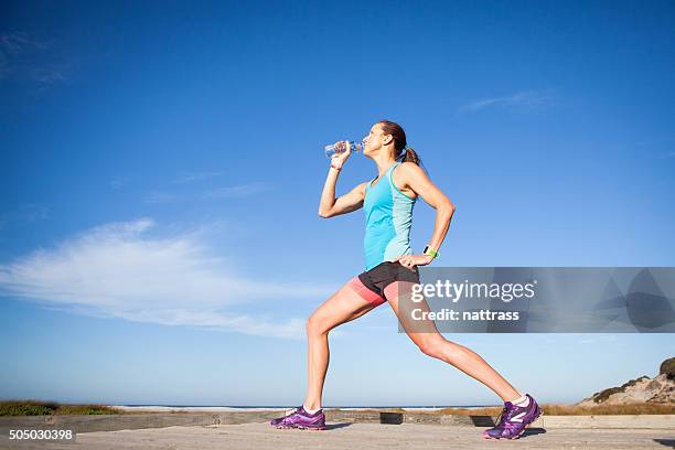 woman runner stretching and drinking water - female muscular calves stockfoto's en -beelden