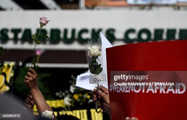 People hold flowers and placards that read "We are not afraid" during a vigil outside the damaged Starbucks coffee shop in central Jakarta on January...