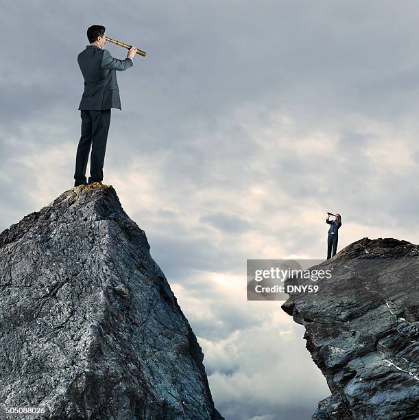 businessman and businesswoman standing on mountaintops looking through spyglass - standing apart stock pictures, royalty-free photos & images