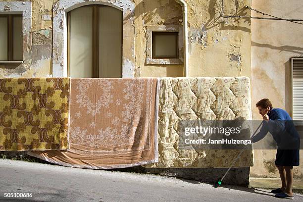 spring cleaning: senior woman sweeping street, blankets airing out, sicily - draped blanket stock pictures, royalty-free photos & images