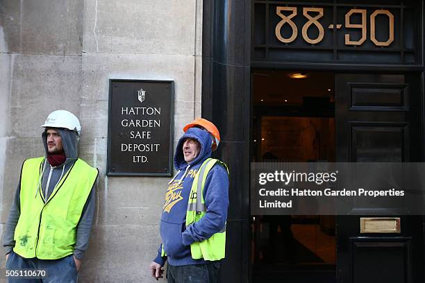 Builders stand next to a sign outside the building housing the underground vault of the Hatton Garden Safe Deposit Company which was raided in what...