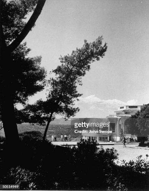 View of Pavilion Eden Roc through the pines on left of promenade running between Hotel du Cap d' Antibes and Eden Roc.