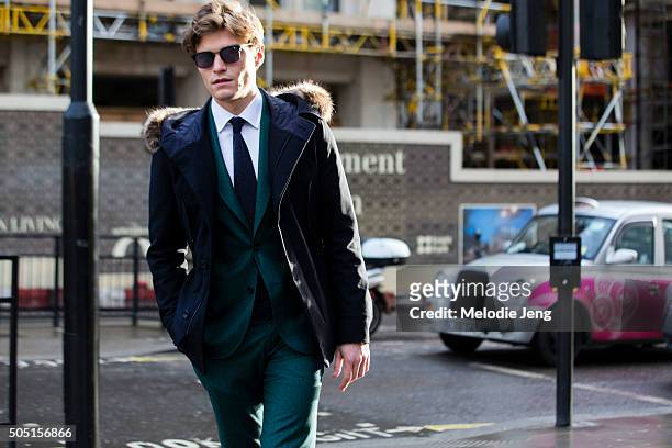 Oliver Cheshire wears Dita sunglasses, a fur-lined blue parka, and a green Hardy Amies suit during The London Collections Men AW16 at The Strand on...