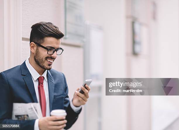 geschäftsmann sms auf das telefon - junger mann liest zeitung stock-fotos und bilder