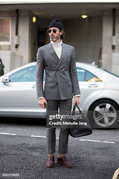 Richard Biedul attends the Richard James show in a gray suit with a white turtleneck, black beanie, maroon oxfords, and a black leather duffle bag...