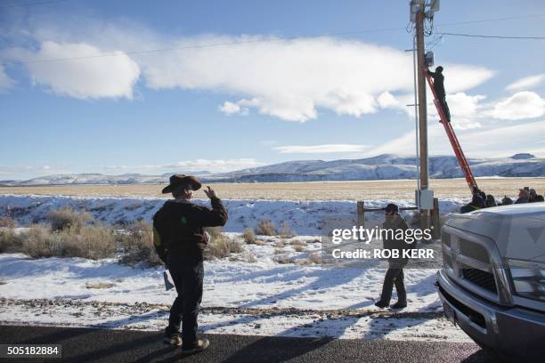 Ryan Bundy, in cowboy hat, observes as a member associated with his group of protestors disables a power pole remote camera location near the...