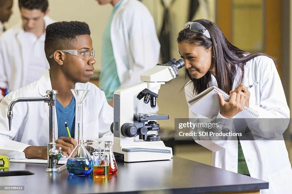 Estudiante de tomar notas mientras examinar portaobjetos de microscopio