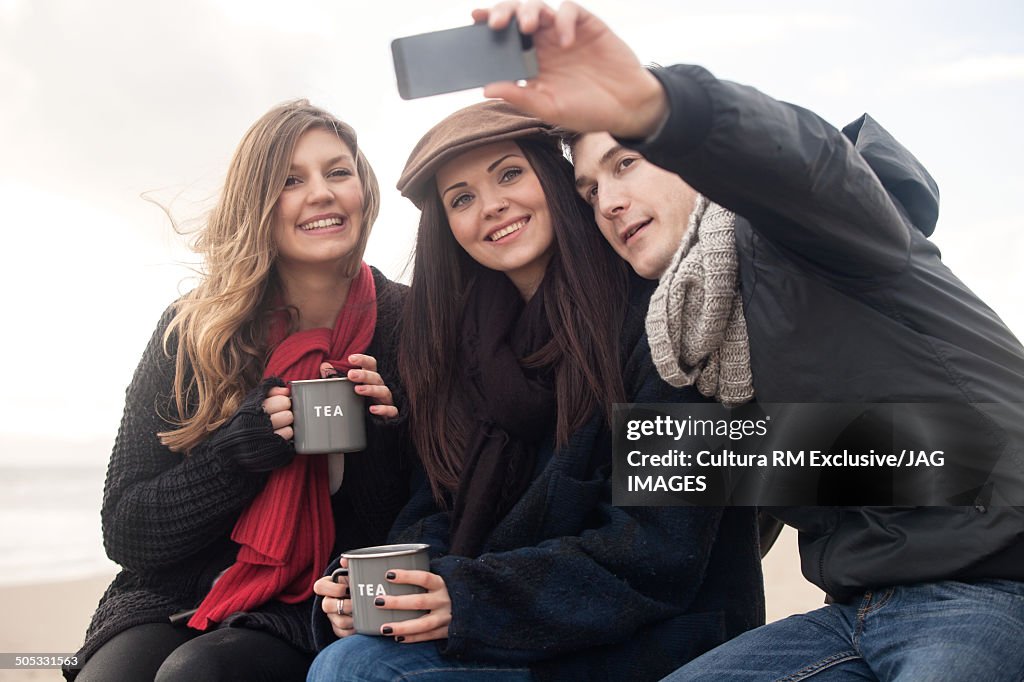 Three friends taking self portrait on smartphone at coast