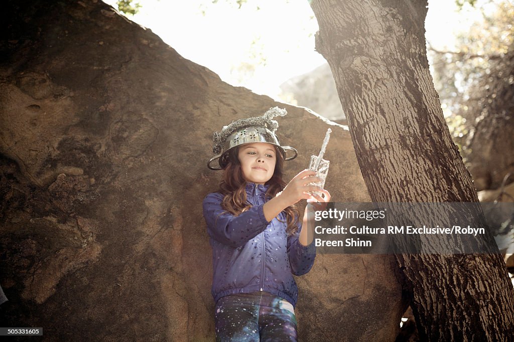 Girl hiding behind rock wearing colander on head