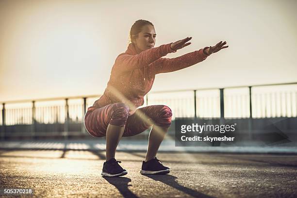 young woman doing squats on a road at sunset. - crouch stock pictures, royalty-free photos & images