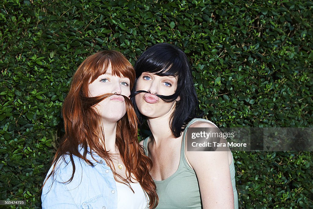 Two women making moustaches with hair