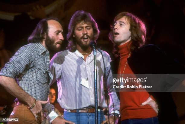 Musician Maurice, Barry, and Robin Gibb of the Bee Gees singing on stage.