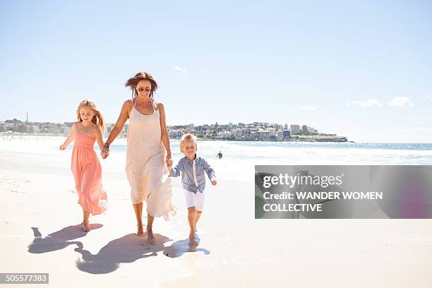 mother and children holding hands along beach - australia city lifestyle stock-fotos und bilder