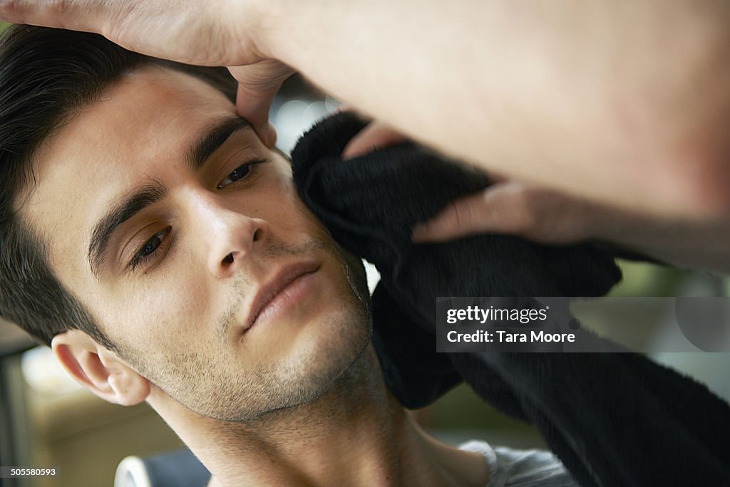 Man wiping face with towel at barber shop