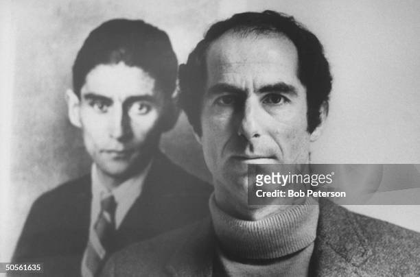 Author Philip Roth posing next to a photo of author Franz Kafka whom he resembles in appearance & whom he owes much in the way of inspiration as a...