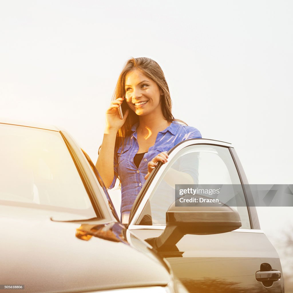 Young woman using cell phone and driving luxury black car