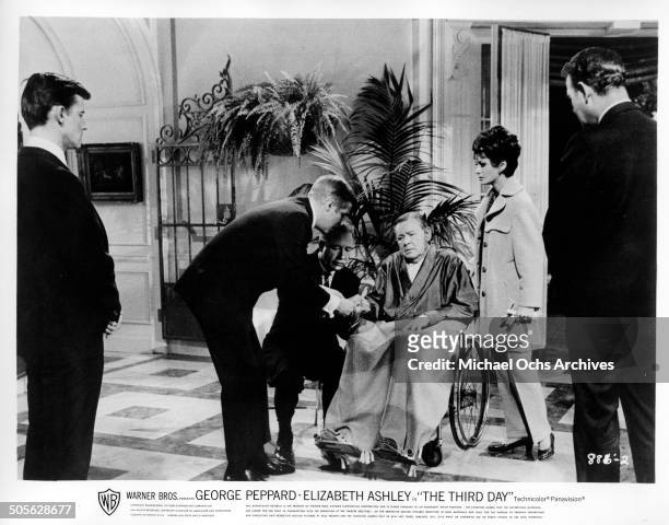 Herbert Marshall in a wheel chair tries to tap out a message for George Peppard as Roddy McDowall and Elizabeth Ashley look on in a scene from the...