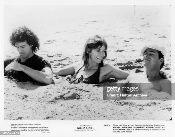 Michael Ontkean, Margot Kidder and Ray Sharkey are buried in the sand, in a scene from the 20th Century Fox movie "Willie & Phil" circa 1980.