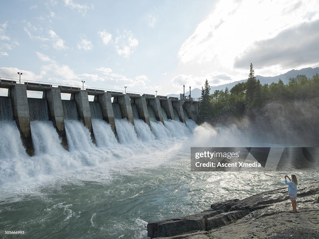 Woman takes pic of water flowing through hydro dam