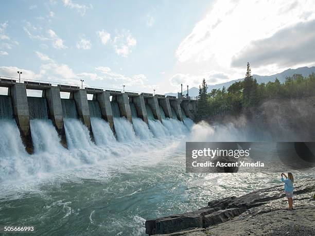 woman takes pic of water flowing through hydro dam - wasserkraft stock-fotos und bilder