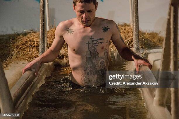 Man with tattoos indicating affiliation with criminal world dives into the freezing waters of Irtysh river on Epiphany on January 19, 2016 in...