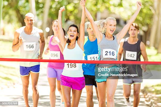 happy female marathon runners crossing finishing line - gift ribbon stockfoto's en -beelden