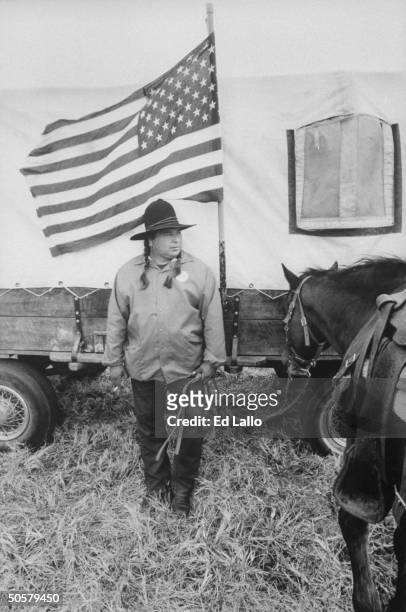 Cherokee indian Archie Mouse standing in front of American flag and covered wagon which he is using to reenact the 1,000 mile journey that his...