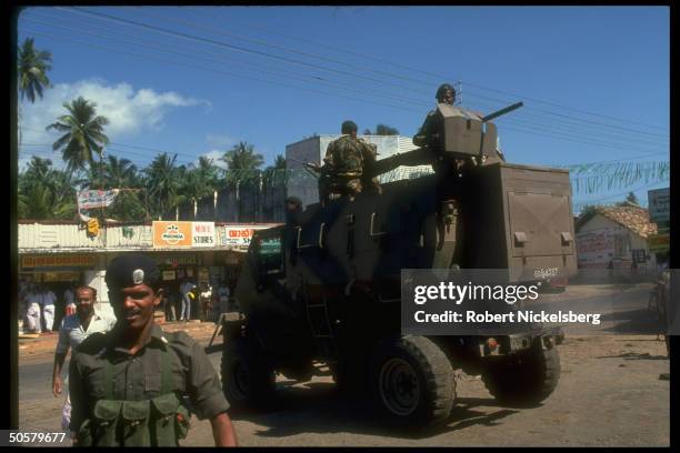 Heavily armed soldiers sit on top of an armored vehicle, rolling down the street.