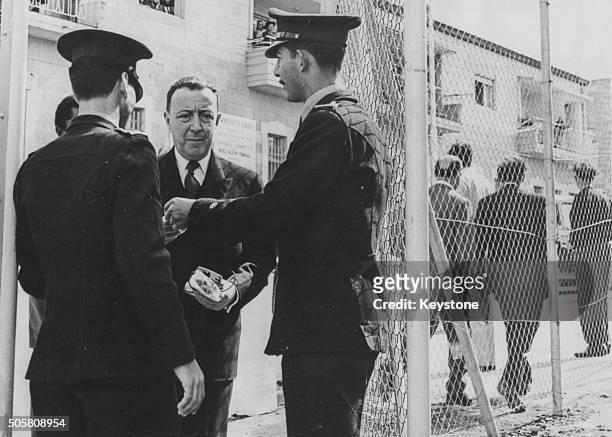 Lord Edward Russell, 2nd Baron Russell of Liverpool, presenting his pass to officers at the entrance of the court buildings during the trial of Nazi...