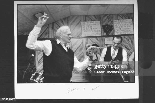 Church leader Dewey Chafin w. Ray Christian handling timber rattlesnakes while trio of musicians play & sing behind them during worship service at...