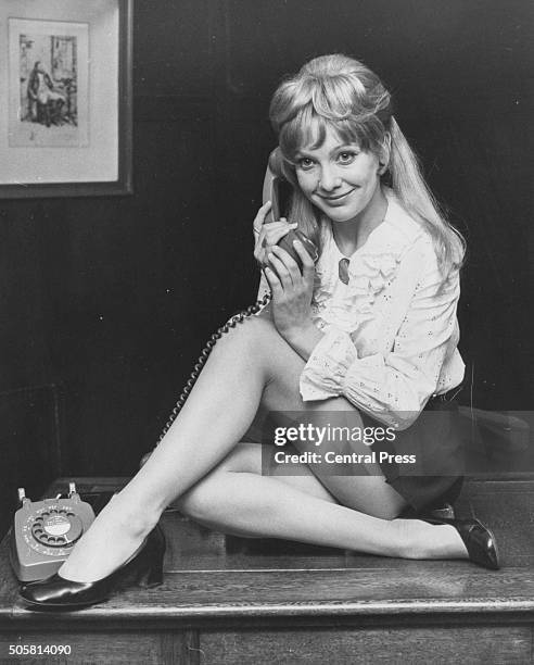 Portrait of actress Jacki Piper sitting on a desk holding a telephone, promoting the role in the play 'The Secretary Bird', at the Savoy Theatre,...