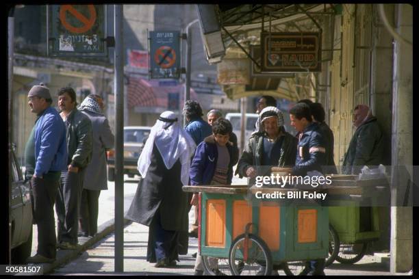 Locals clustering around vendor's cart in fore of shutterered shops closed in intifada-inspired gen. Strike; Ramallah, Israeli-occupied West Bank.