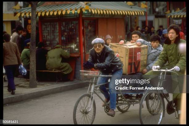 Pedicab driver engaged by passengers carrying Toshiba TV carton on their laps.