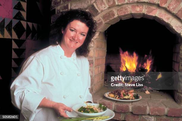 Chef Lydia Shire holding bowl of green curry lobster soup, lobster salad sandwich on plate on hearthstones in front of fire; Biba restaurant.