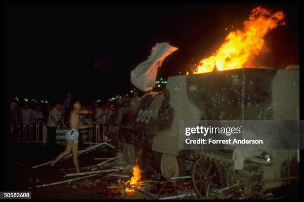 Man in shorts hurling white cloth at burning tank while men in bkgrd. Watch during student pro-democracy protests in Tiananmen Sq.