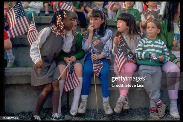 Patriotic little Girl Scouts poised w. Flags, celebrating Flag Day, w. Little boy leaning jauntily in their midst, snacking.